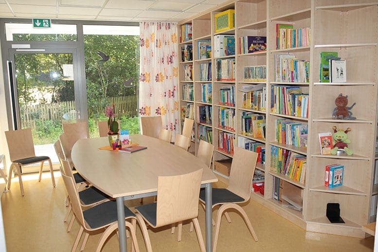 Leseecke mit ovalem Tisch, Holzstühlen und raumhohem Bücherregal neben der Glastür zum Garten