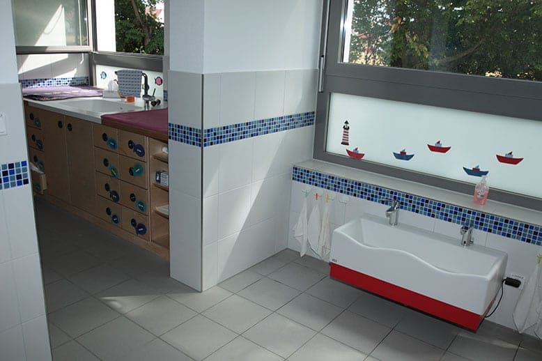 Kinderwaschraum mit niedrigem Waschtrog, blauem Mosaikband und Bootsmotiven am Fenster