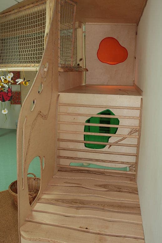 Aufgang der Holzkletterlandschaft mit Sprossen, farbigen Plexiglasfenstern und Netzbrüstung