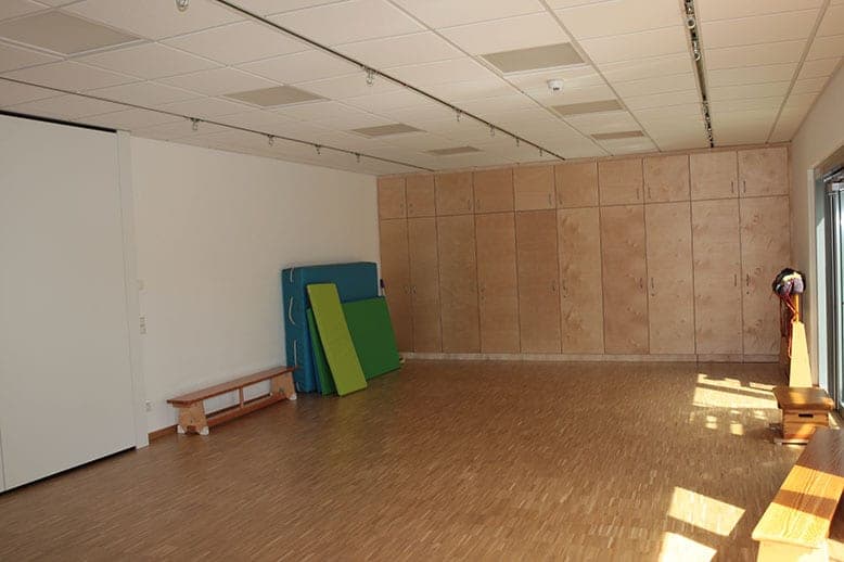 Mehrzweckraum mit Parkettboden, Turnmatten, Langbank und wandhohen Einbauschränken aus Holz