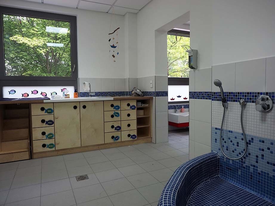 Wickelraum mit Wickelkommode, gefliester Duschwanne aus blauem Mosaik und Durchgang zum Waschraum