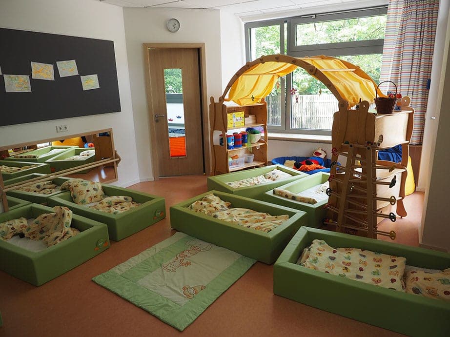 Ruheraum der Krippe mit grünen Schlafmulden, gelbem Spielbogen und Kletterleiter