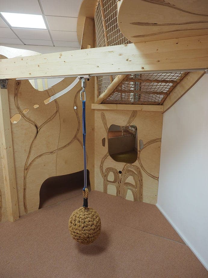 Seil mit Knotenball unter der Netzebene, dahinter Holzwände mit eingefrästen Linien und Durchblick