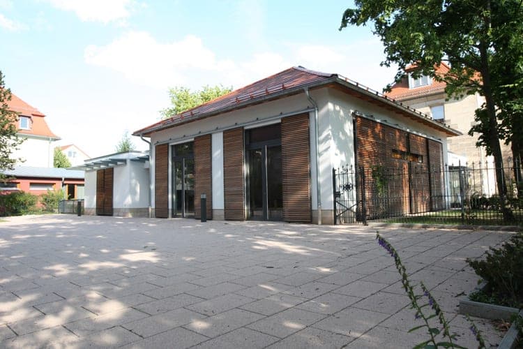Pavilion with a hipped roof and timber-louvre shutters on the paved forecourt, a wrought-iron gate to the right