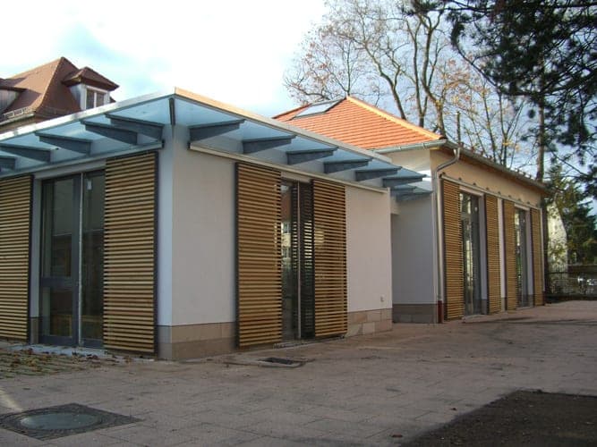 New wing and pavilion of the parish centre in autumn with light-coloured timber-louvre shutters and glass canopy