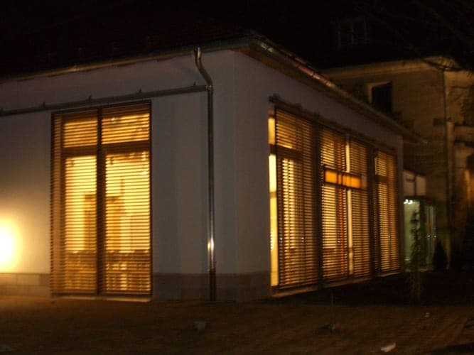 Night view of the pavilion with warmly lit rooms behind closed louvre shutters