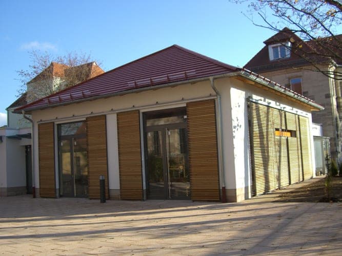 Pavilion with a red hipped roof, glazed doors and timber-louvre shutters in autumn sunshine