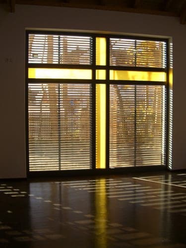 Interior with a window front whose yellow-glazed strips form a cross, light reflected on the dark floor