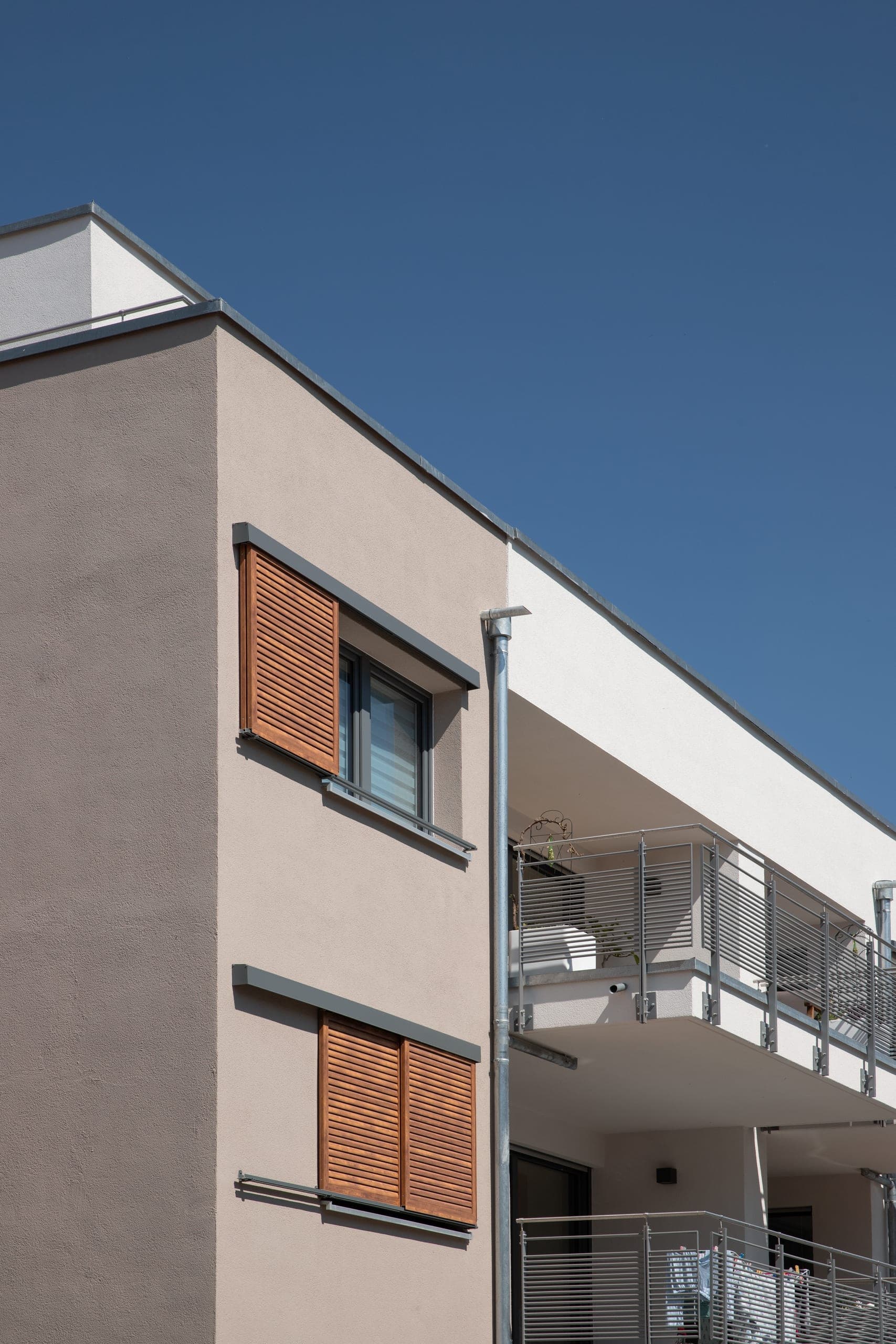Building corner with wood-coloured sliding shutters at the windows and balconies with metal railings alongside