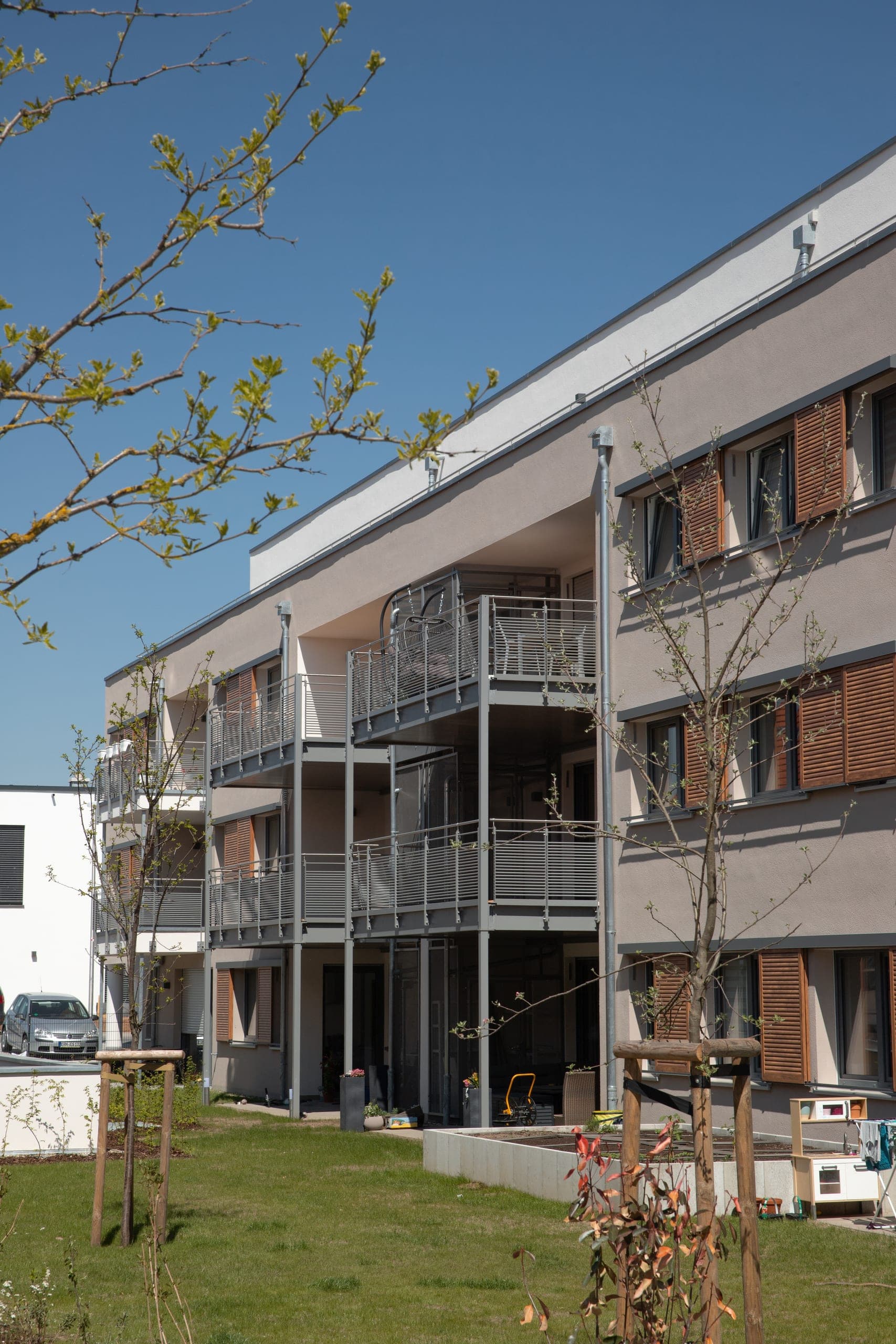 Garden side with projecting steel balconies and wood-coloured sliding shutters on the rendered façade