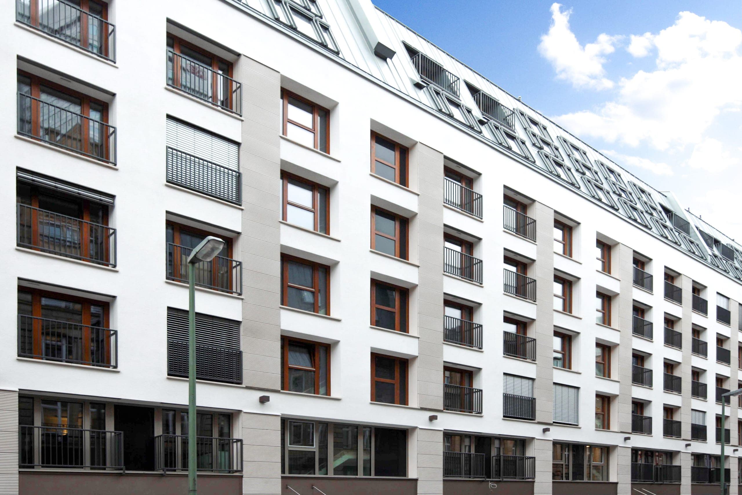 Helle Straßenfassade mit Holzfenstern, französischen Balkonen und Gauben im Metalldach