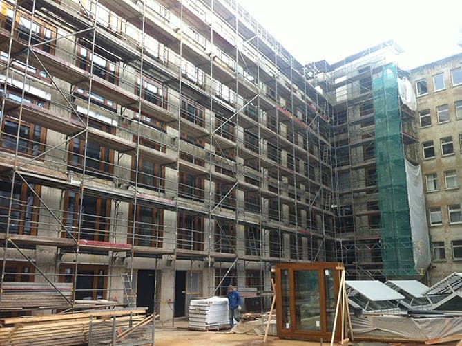 Innenhof während der Kernsanierung mit eingerüsteter Fassade und neuen Fensterelementen am Boden