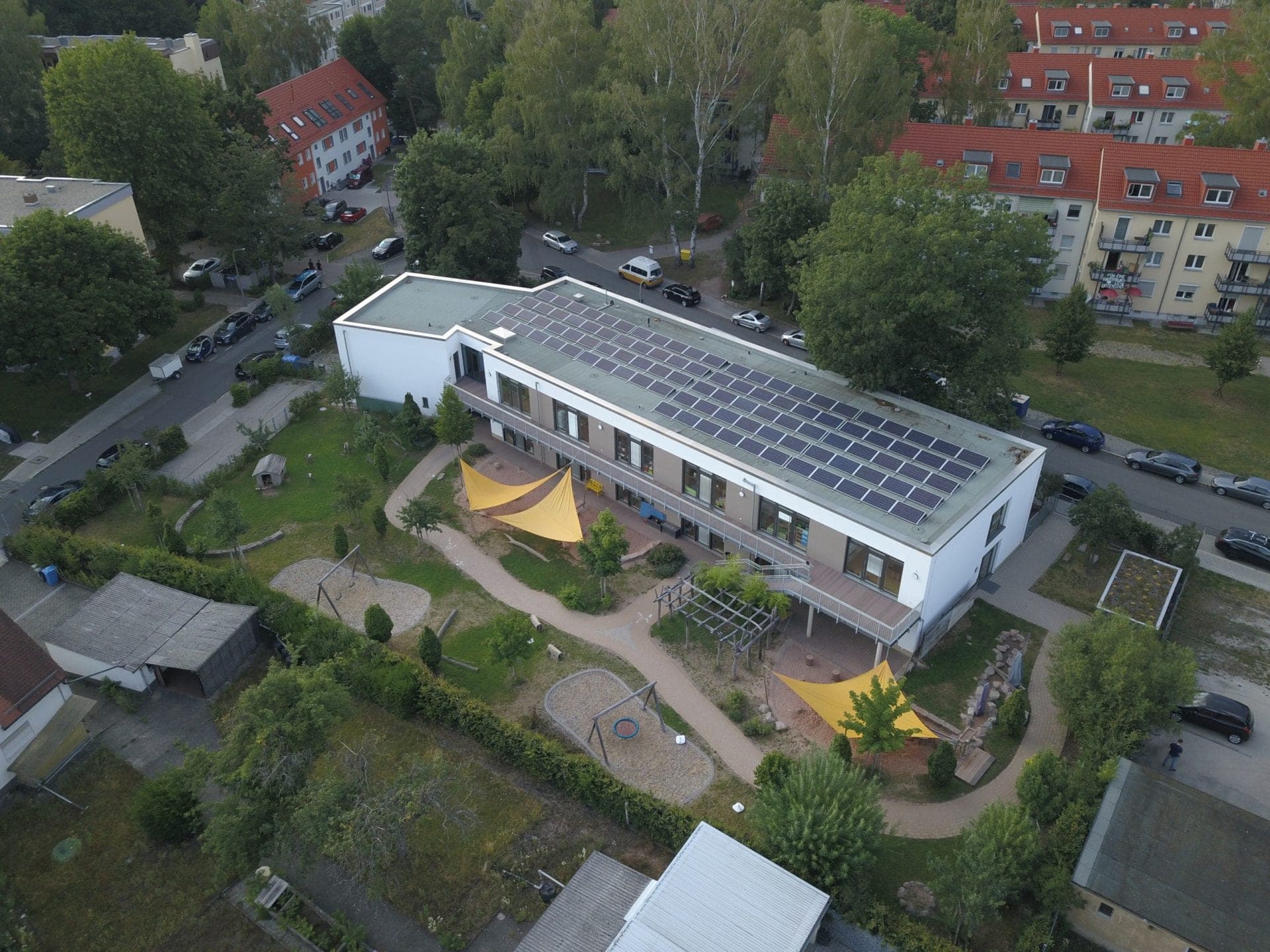 Aerial view among mature trees with the photovoltaic roof, external walkway and play areas with swings and sun sails