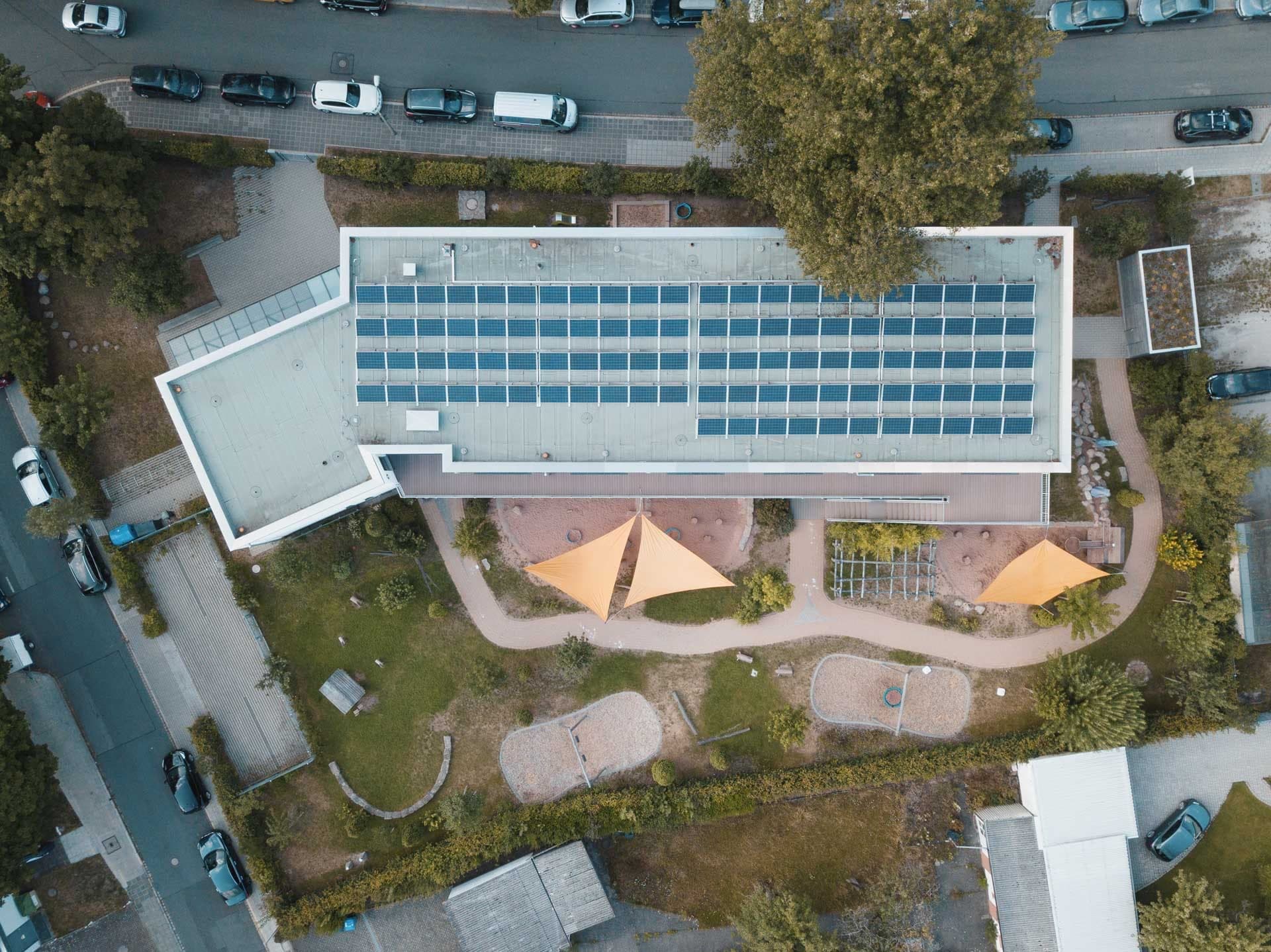 Overhead aerial view of the flat roof with photovoltaic array above the play garden with sand areas and sun sails