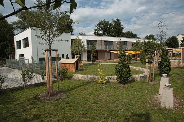 Play garden with a wooden playhouse and natural stone wall, with the upper-floor walkway behind