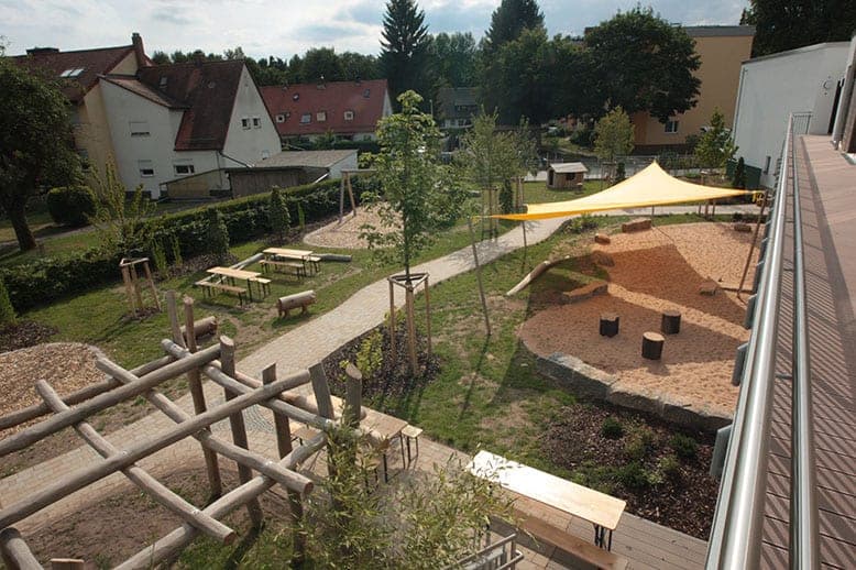 View from the walkway over the play garden with sandpit, sun sail, picnic sets and a timber climbing frame