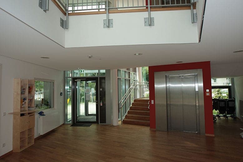 Two-storey foyer with timber floor, entrance door, staircase and a lift set against a red wall panel