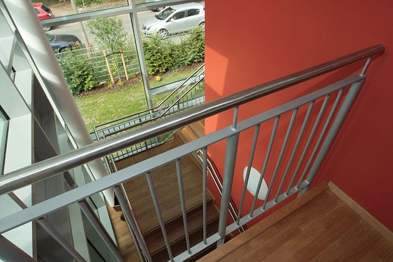 Staircase with timber treads and metal railing against a red wall, with a view through the glazing to the street