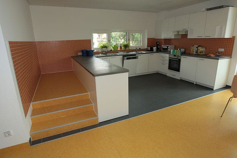Kitchen with white fitted units and orange tiles beside a stepped seating platform