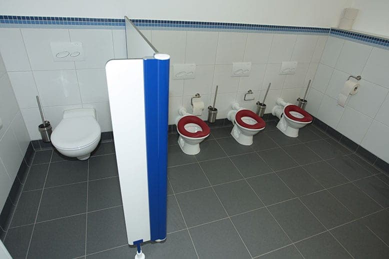 Day-care washroom with three children's toilets with red seats and an adult WC behind a partition