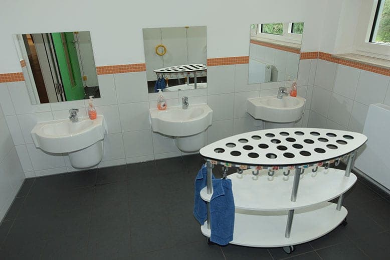 Washroom with three low basins below mirrors and a mobile towel trolley