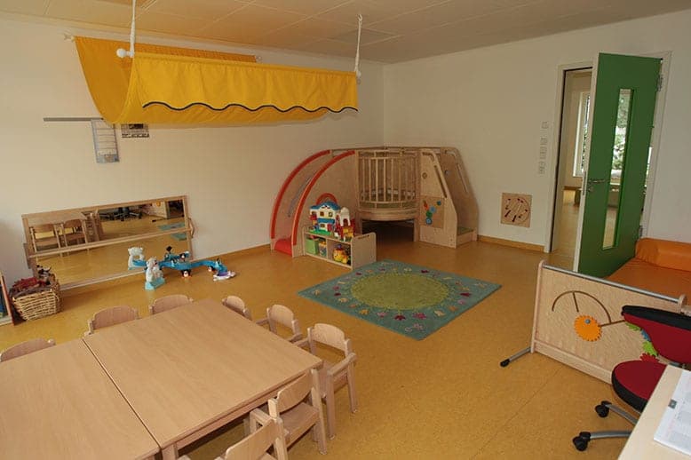 Group room in Nuremberg with children's tables, a play platform with slide, a rug and a green door