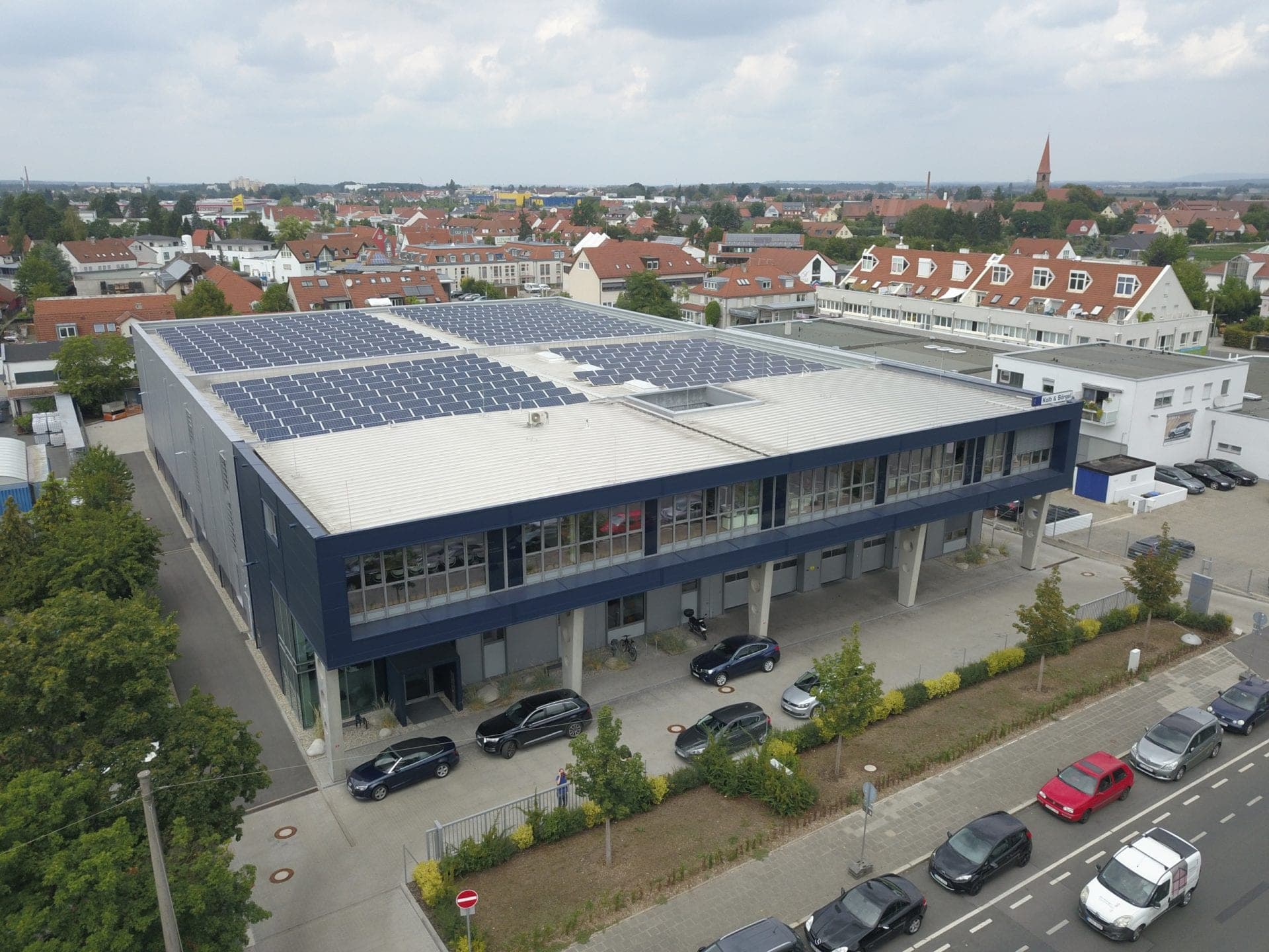 Aerial view across the hall roof with solar panels towards the surrounding housing with red tiled roofs
