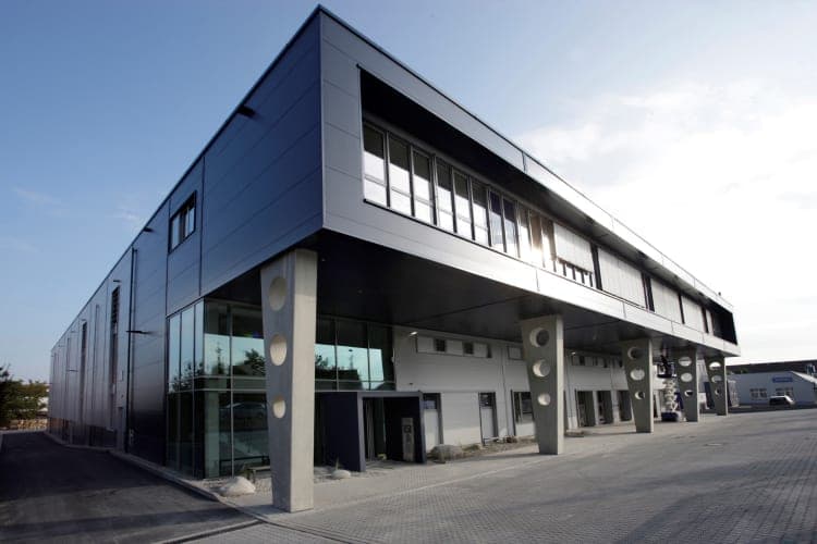 Building corner with dark metal cladding and concrete columns with round cut-outs beneath the office floor