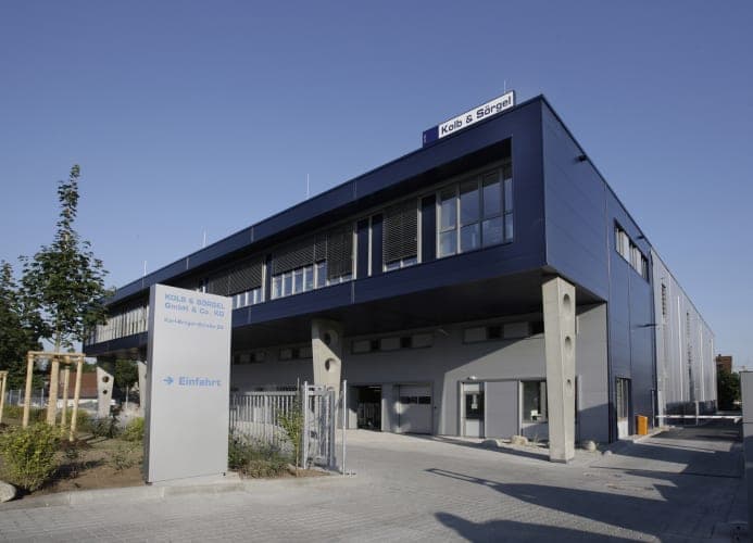 Entrance drive with the company sign and a view of the dark blue façade of the Fürth headquarters