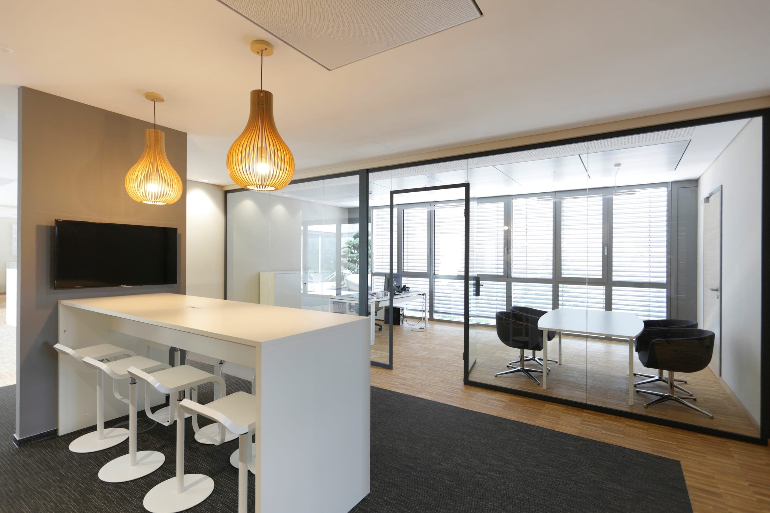 Break-out area on the office floor with a standing table, stools and a glazed meeting room
