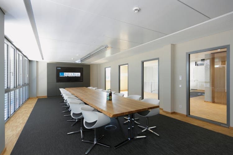 Meeting room with a long wooden table, white chairs and a screen on the end wall