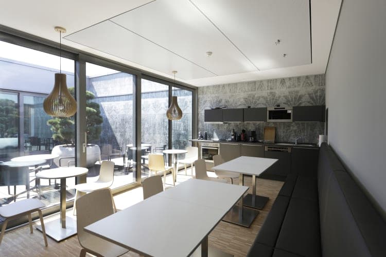 Kitchenette with dark fitted units, bench seating and tables in front of the glazing to the courtyard