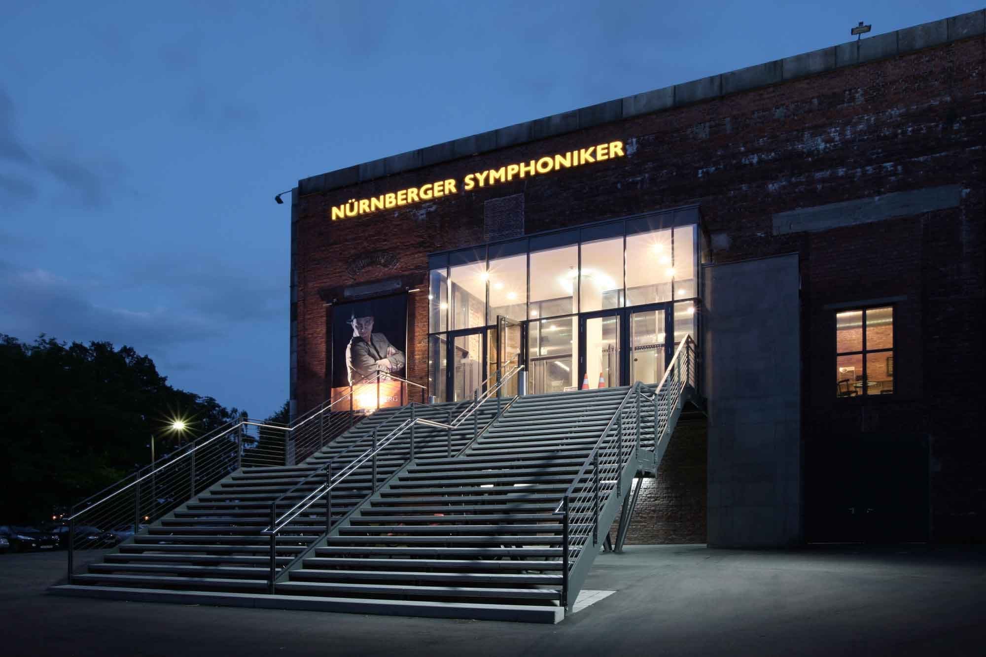 Glazed entrance box with open staircase set into the brick wall of the north façade at dusk
