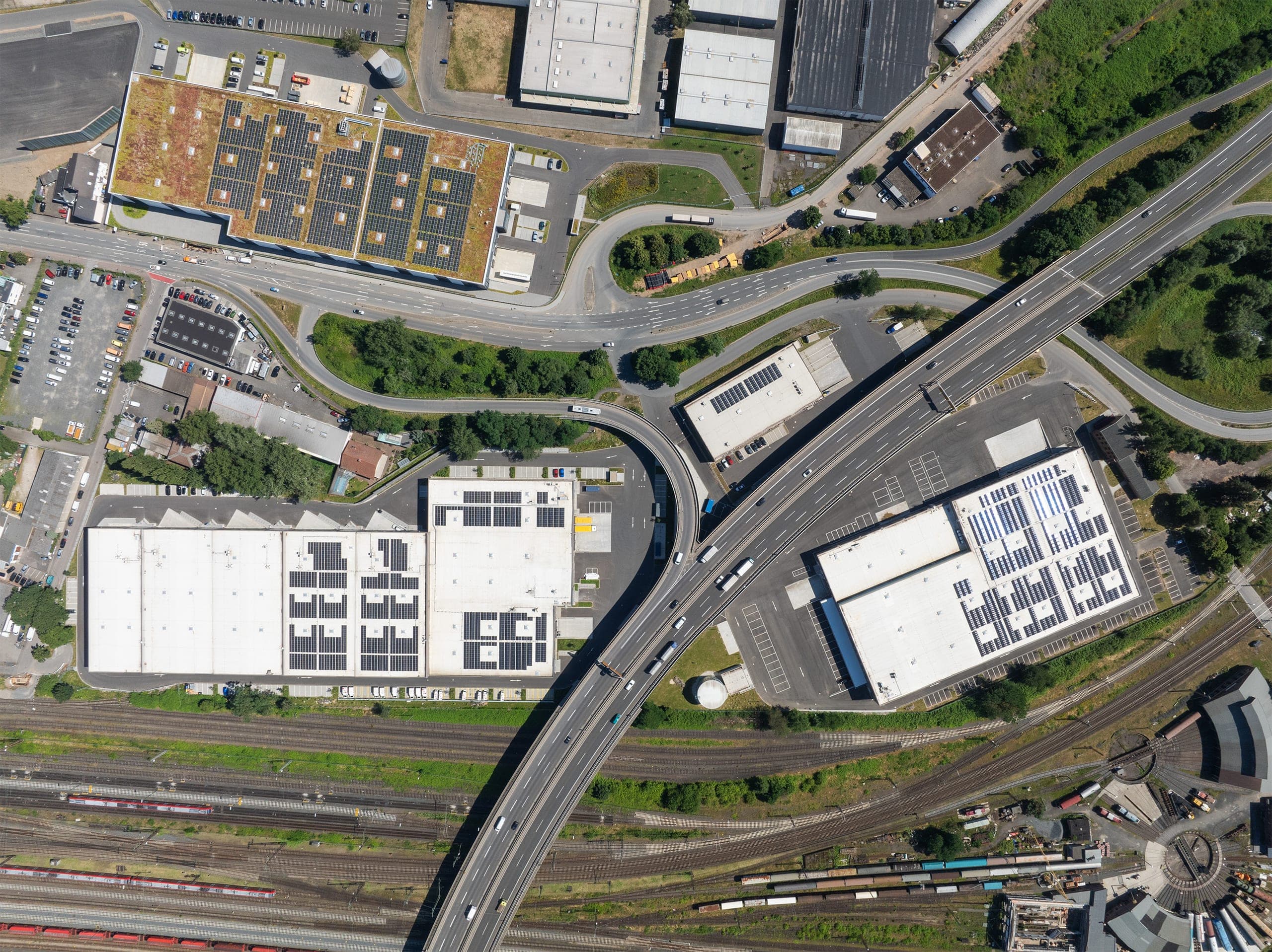 Senkrechtluftbild der Hallen mit Solarmodulen am Straßenkreuz, unten Gleisanlagen mit Ringlokschuppen