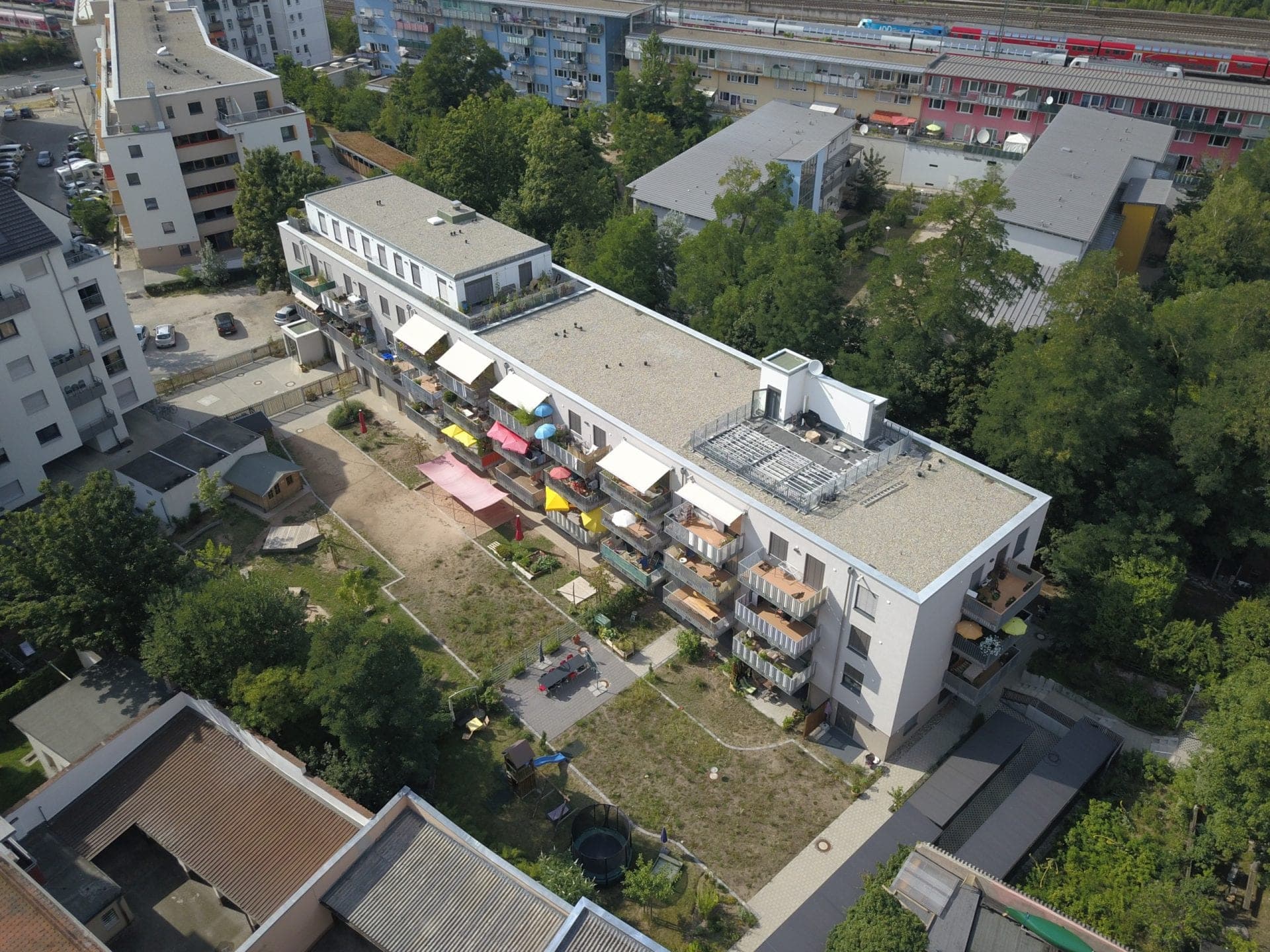 Schräges Luftbild des Wohnhauses mit Dachterrasse, Gartenhof, Sandflächen und Spielgeräten