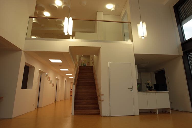 Foyer mit offener Galerie, Glasbrüstung, Holztreppe und Pendelleuchten im Mehrgenerationenhaus