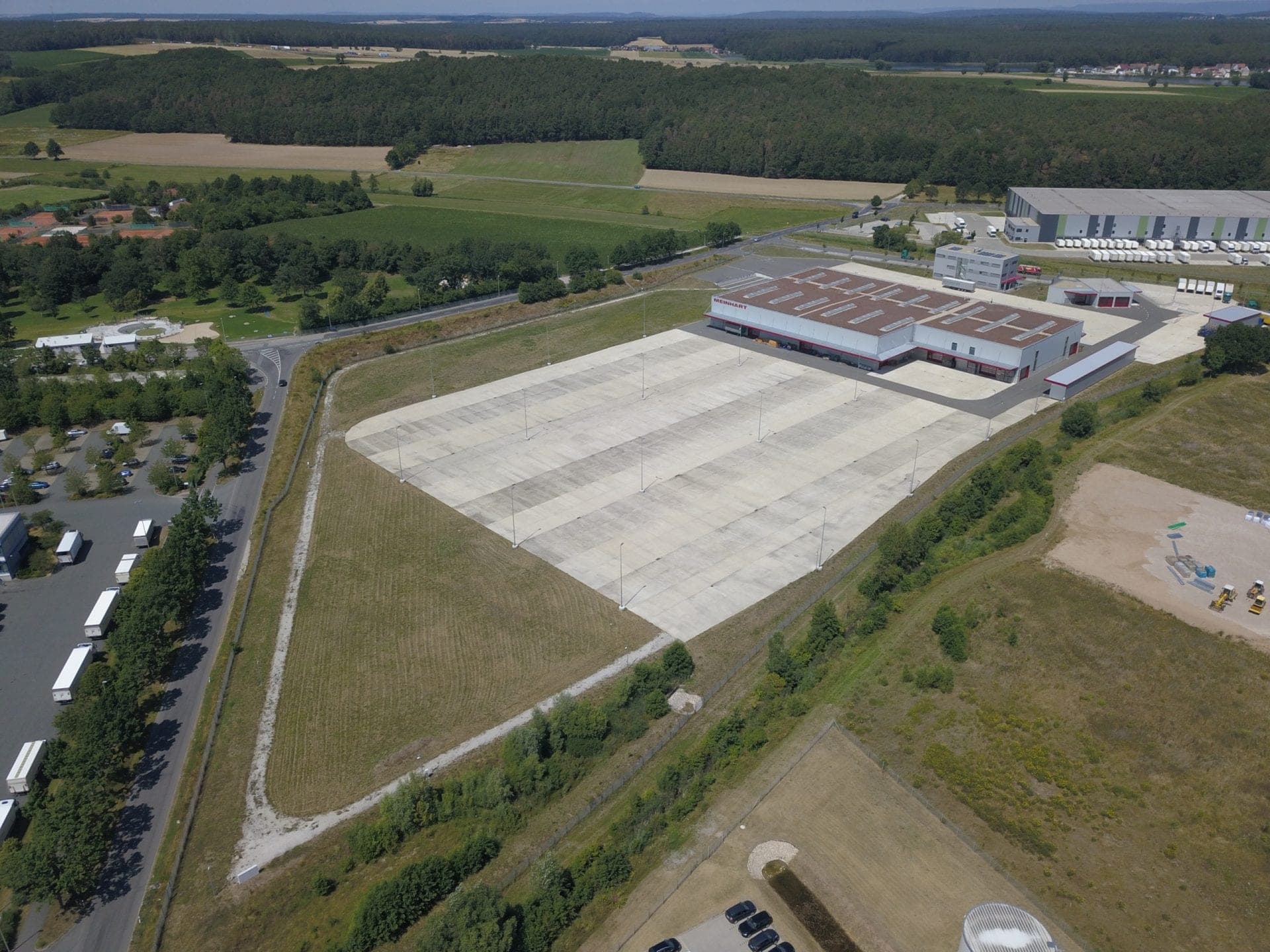 Aerial view of the site with a large concrete yard, the business park and woodland in the background