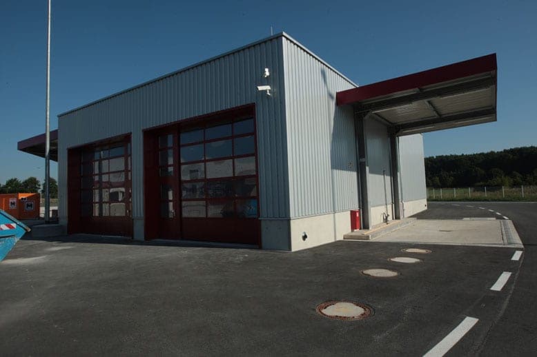 Workshop with two red doors and the adjoining canopy of the vehicle wash bay in evening light