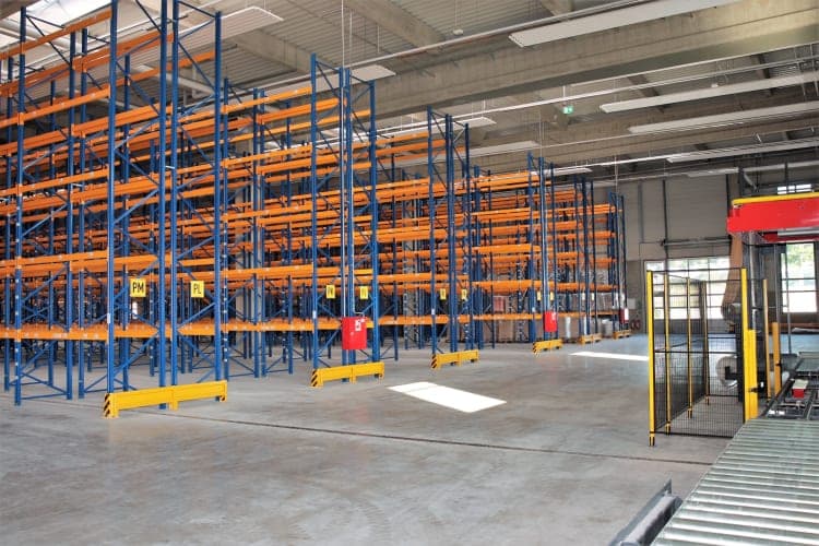 Interior of the logistics hall with tall blue and orange pallet racking and conveyor equipment
