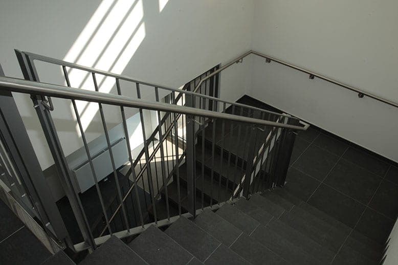Staircase in the office building with steel railings, dark tiled flooring and stripes of light on the wall