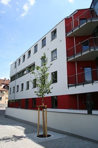Rückseite mit rot-weißer Fassade, Balkonen und frisch gepflanztem Baum vor einer Sockelmauer