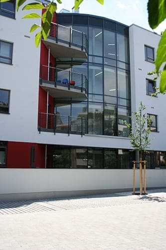 Gerundetes verglastes Treppenhaus mit Balkonen an der Hofseite, davor ein junger Baum