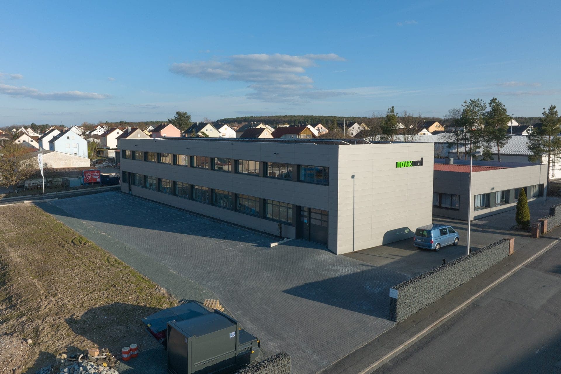 Aerial view of the light-coloured two-storey office façade with ribbon windows, entrance and paved forecourt