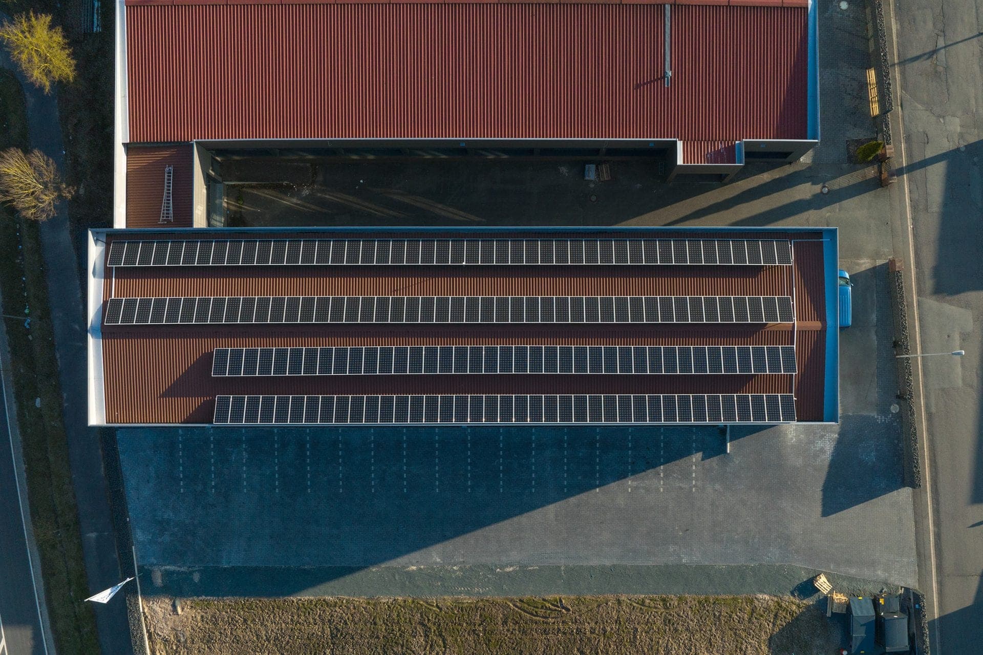 Bird's-eye view straight down onto the rows of solar panels and the red profiled metal roof of the adjoining hall