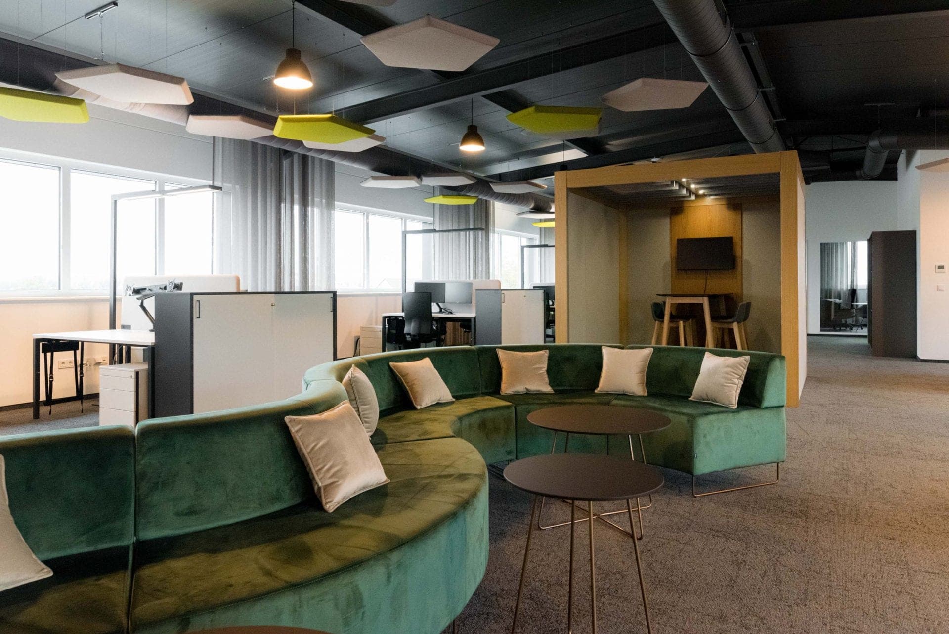 Office lounge with a curved green sofa and a timber-framed meeting pod
