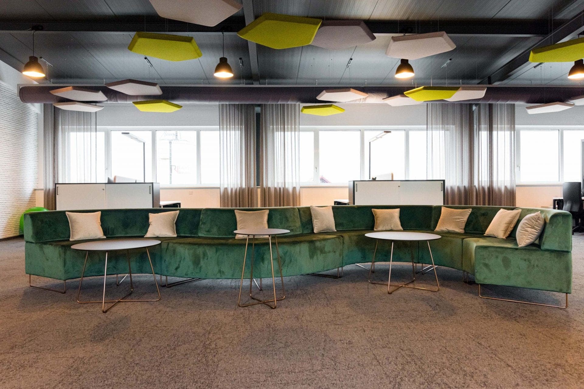 Curved green seating landscape with round side tables in front of the window front with sheer curtains