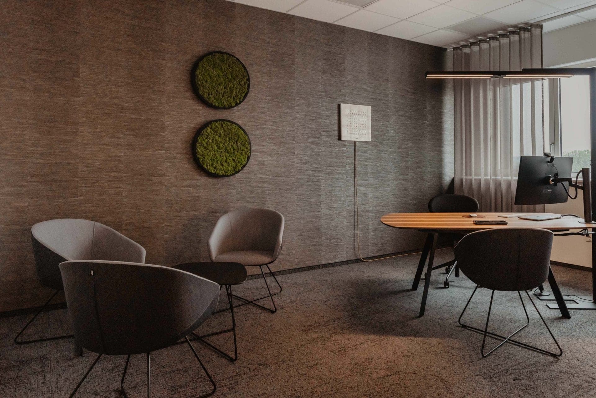 Private office with a desk, a group of armchairs and two round moss panels on the textured wall