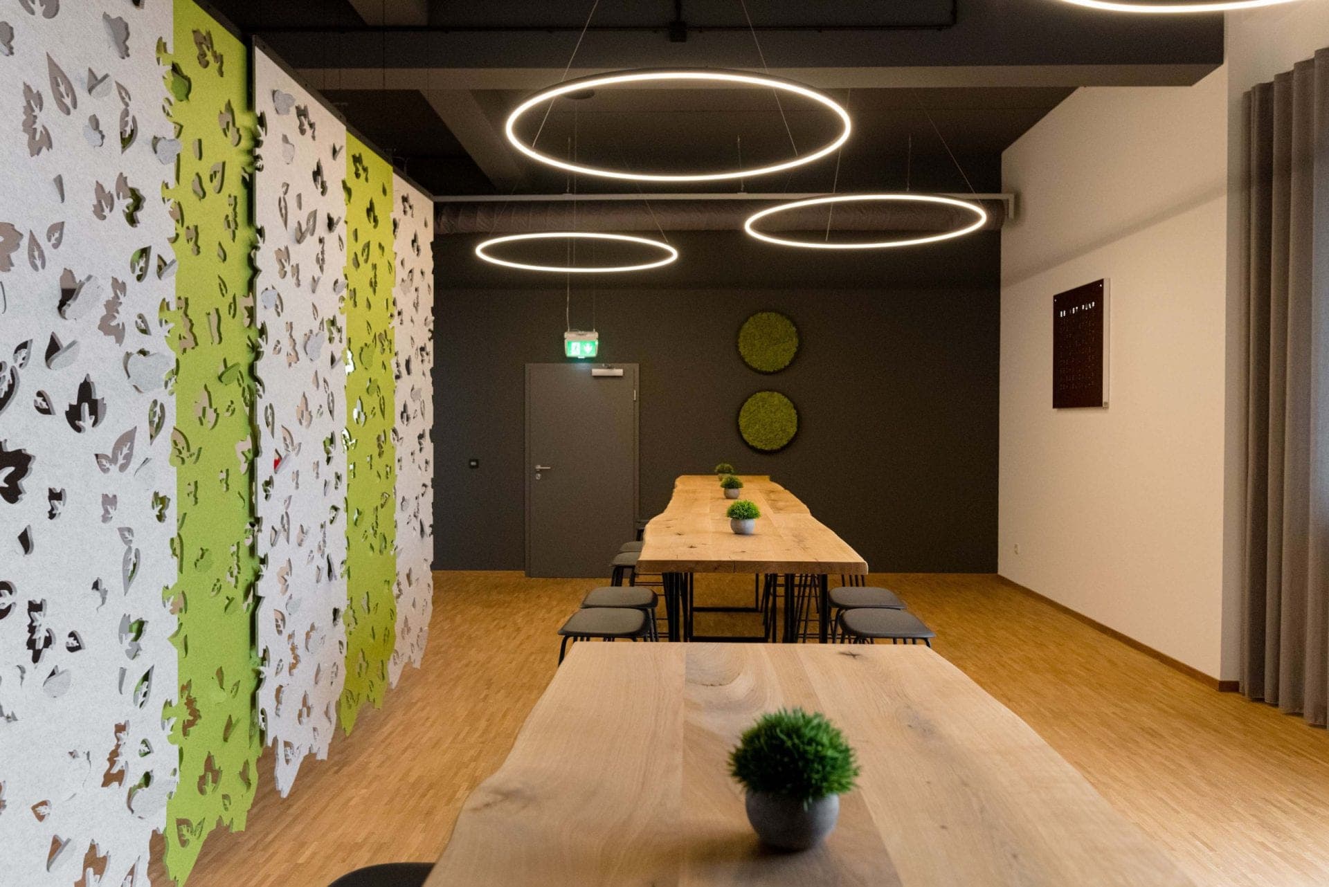 View along the wooden tables in the break room towards two round moss panels on the dark end wall