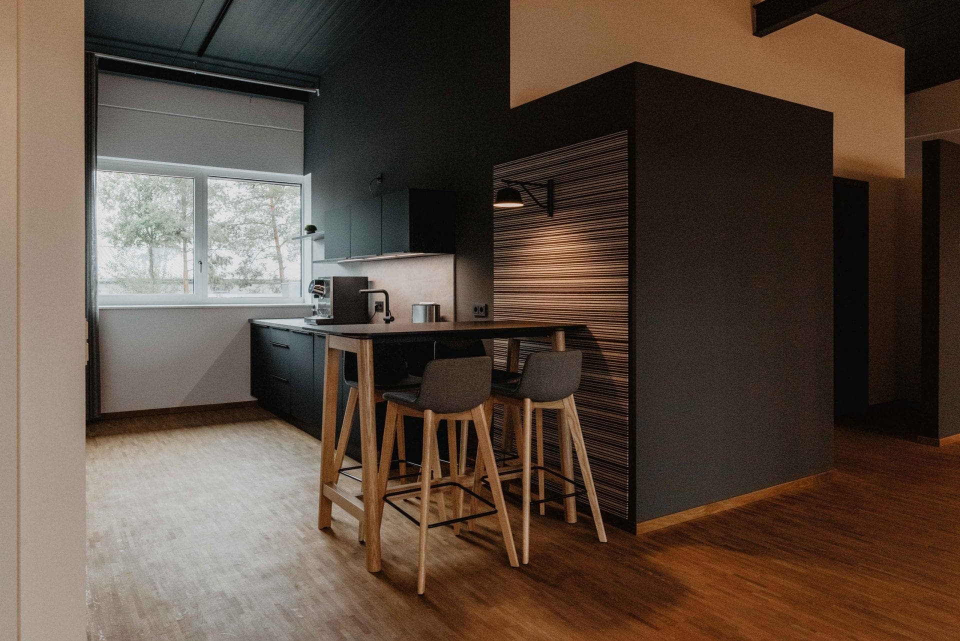 Kitchenette with dark units and a standing table in front of a striped timber wall cladding
