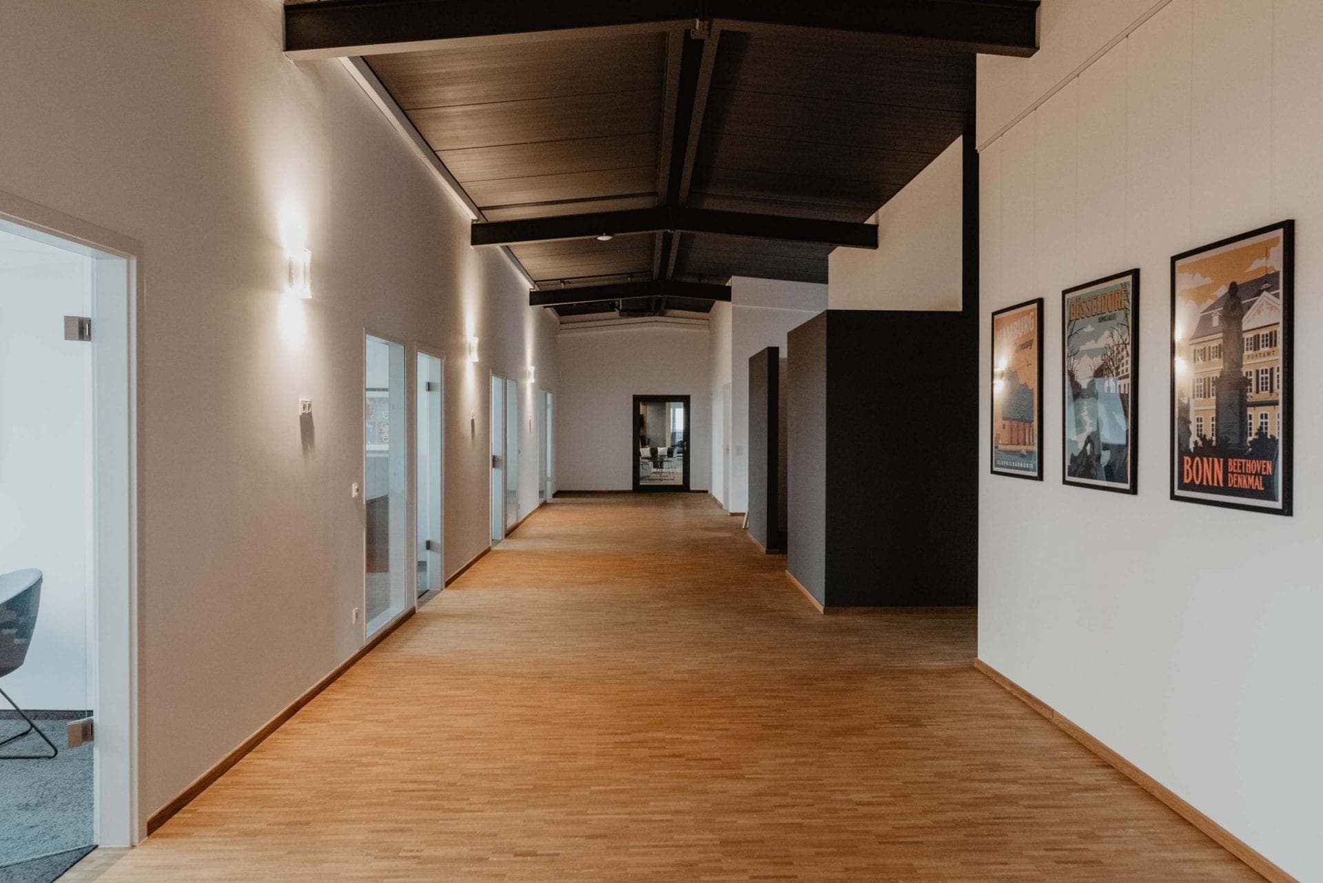 Upper floor corridor with a dark beamed ceiling, glazed office doors and framed city posters